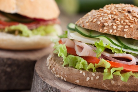 Delicious ham, cheese and salami sandwich with vegetables, lettuce, cherry tomatoes in natural setting with wooden backgroundの写真素材