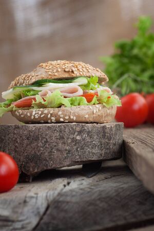 Delicious ham, cheese and salami sandwich with vegetables, lettuce, cherry tomatoes in natural setting with wooden backgroundの写真素材
