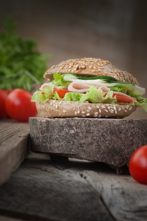 Delicious ham, cheese and salami sandwich with vegetables, lettuce, cherry tomatoes in natural setting with wooden backgroundの写真素材