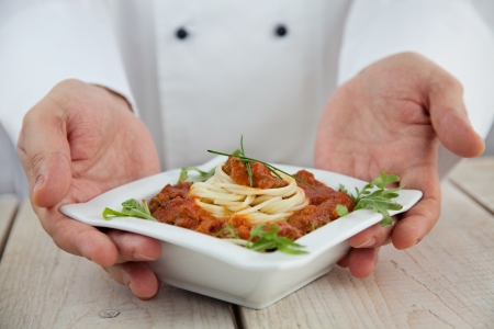Male chef in restaurant kitchen is garnishing and preparing pasta dishの写真素材
