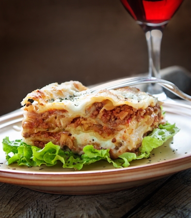 Italian cuisine. Freshly baked homemade lasagna with minced meat and cheese served on a piece of lettuce and red wine.の写真素材