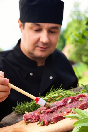 Cooking ingredients: marinated meat,oil,vinegar, herbs and vegetables. Chef is carving and marinating meat.の写真素材