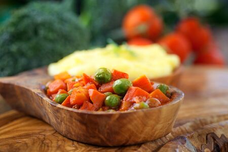 Vegetarian dinner. Corn meal or polenta with peas and carrots in sauce. Broccoli and tomato in the backgroundの写真素材