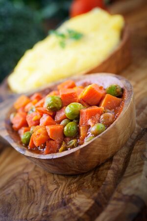Vegetarian dinner. Corn meal or polenta with peas and carrots in sauce. Broccoli and tomato in the backgroundの写真素材