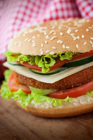 Junk food concept. Deep fried chicken or fish burger sandwich with lettuce, tomato, cheese and cucumber on wooden background.の写真素材