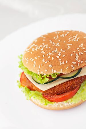 Junk food concept. Deep fried chicken or fish burger sandwich with lettuce, tomato, cheese and cucumber on wooden background.の写真素材