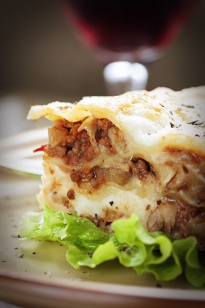 Italian cuisine. Freshly baked homemade lasagna with minced meat and cheese served on a piece of lettuce and red wine.の写真素材