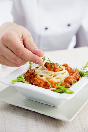 Male chef in restaurant kitchen is garnishing and preparing pasta dishの写真素材