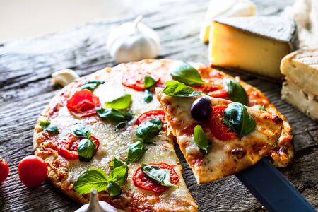 Pizza on wood with ingredients. Pizza with cheese, tomatoes and basil. Rustic italian pizza