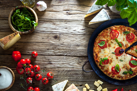 Pizza on wood with ingredients. Pizza with cheese, tomatoes and basil. Rustic italian pizzaの写真素材