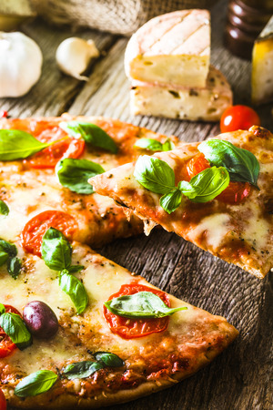 Pizza on wood with ingredients. Pizza slice with cheese, tomatoes and basil. Rustic italian pizzaの写真素材