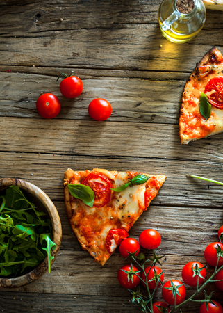 Pizza slice on wood with ingredients. Pizza with cheese, tomatoes and basil. Rustic italian pizzaの写真素材