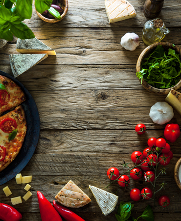 Pizza on wood with ingredients. Pizza with cheese, tomatoes and basil. Rustic italian pizzaの写真素材