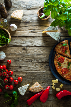 Pizza on wood with ingredients. Pizza with cheese, tomatoes and basil. Rustic italian pizzaの写真素材