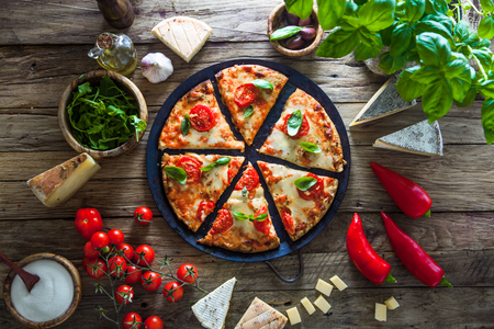 Pizza on wood with ingredients. Pizza with cheese, tomatoes and basil. Rustic italian pizzaの写真素材