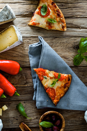 Pizza slice on wood with ingredients. Pizza with cheese, tomatoes and basil. Rustic italian pizzaの写真素材