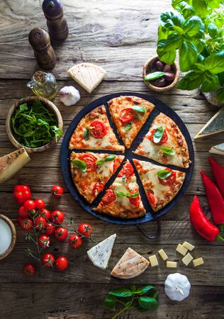 Pizza on wood with ingredients. Pizza with cheese, tomatoes and basil. Rustic italian pizzaの写真素材