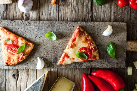 Pizza slice on wood with ingredients. Pizza with cheese, tomatoes and basil. Rustic italian pizzaの写真素材