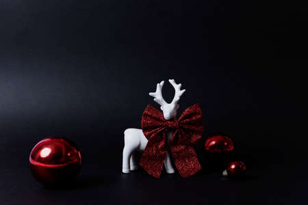 White ceramic deer with a red sparkly bow and red Christmas balls on black dark backgroundの写真素材