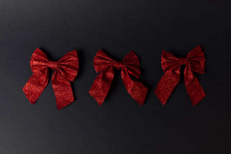 Three red Christmas sparkly bows in a row on black dark backgroundの写真素材