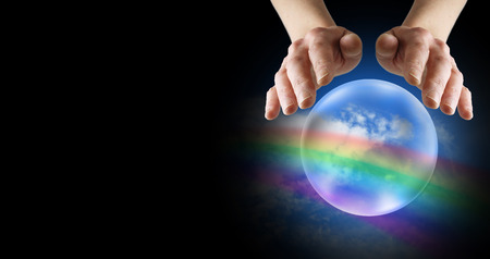 Clairvoyant hands over crystal ball with rainbow and blue sky on a black banner backgroundの写真素材