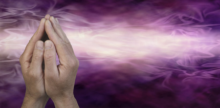 Cupped Hands in Prayer Position -  Male hands cupped together in prayer position on a dark purple and light pink energy streaming misty graduated background with plenty of copy space on the right hand sideの写真素材