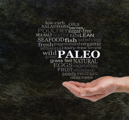 Consider The Paleo Diet - Chunky male hand with cupped palm  and a PALEO word cloud floating above on a dark stone cave wall effect background with copy spaceの写真素材