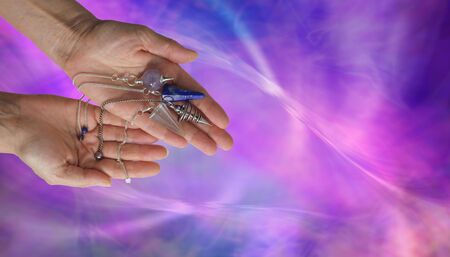 Offering 4 different dowsing pendulums - female dowser holding four radionics pendants in an...