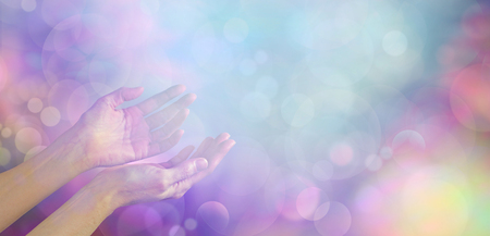 Supernatural Phenomenon - female healing hands gently cupped up facing towards an ethereal blue white light orb on a muted multicolored bokeh background with plenty of copy spaceの写真素材