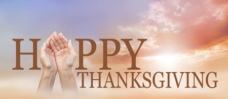 Sharing a Happy Thanksgiving -  wide autumnal sunset sky background with a pair of cupped female hands making the A of HAPPY with THANKSGIVING below and copy space aboveの写真素材