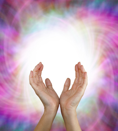 Vortex Energy Field - Female energy worker with hands outstretched and open upwards sensing white healing energy on pink vortexing multicolored energy formation backgroundの写真素材