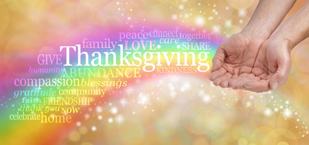 Celebrate Thanksgiving - Male hands cupped with a bright rainbow flowing from behind and a THANKSGIVING word cloud arcing across on a warm golden sparkling background with copy spaceの写真素材