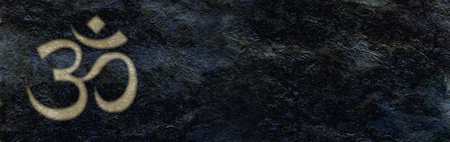 Golden Om engraved on rough black stone banner background - a pale gold etched OM symbol in the left corner against jet black shiny wet look wide stone wallの写真素材