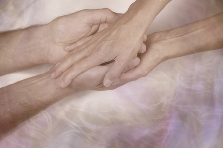 Giving a gentle blessing - cupped male hands being held and blessed by female hands on a wispy smoke effect background and copy space belowの写真素材