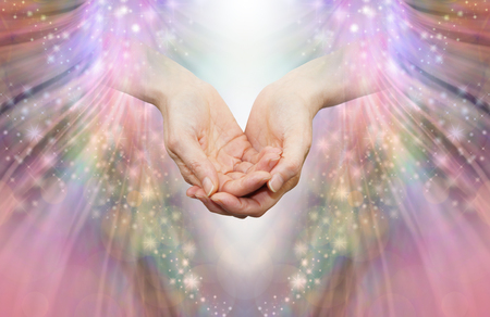 Energy healer receiving high vibrational energy - female cupped hands and shaft of white light against an angelic pink and sparkle energy flow backgroundの写真素材