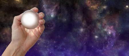 Crystal Gazing Deep Space background - female hand holding a crystal ball with a white light against a wide night sky deep space background with copy spaceの写真素材