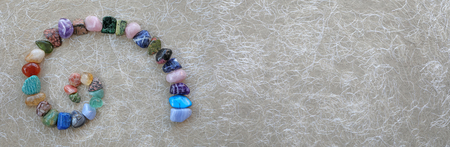 Crystal Fibonacci Spiral Background Banner -  carefully arranged crystal healing gemstones in spiral shape on left against rustic buff coloured fibre paper with copy space on rightの写真素材