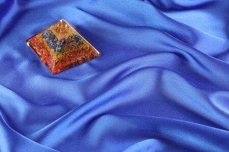 Orgone Pyramid on Cobalt Blue Silk background - orgone showing seven chakra layers in top left corner sitting on gently undulating royal blue silk material backgroundの写真素材