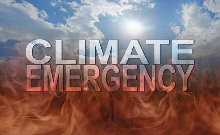 Our precious earth is subject to a CLIMATE EMERGENCY -  blue sun and sky background deteriorating into dark flames as earth burns with the transparent graphic words CLIMATE EMERGENCY in the centreの写真素材