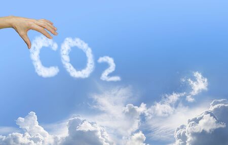 Take responsibility for your CO2 emissions - female hand reaching out to clouds reading CO2 against a blue sky background with fluffy clouds at the bottomの写真素材
