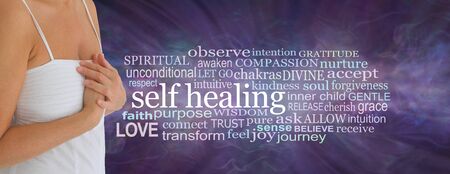 Female Self Healing Word Tag Cloud -  mature woman in white dress with hands crossed over heart beside a SELF HEALING word cloud against a wispy purple ethereal energy backgroundの写真素材