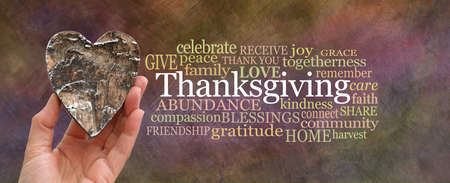 Put some love into Thanksgiving Word Cloud concept - hand holding a rustic brown wooden heart beside a THANKSGIVING word cloud on oil painted warm coloured backgroundの写真素材