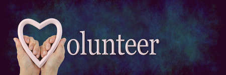 Volunteer with heart message banner  - female hands holding a pale pink heart frame against a dark blue rustic background with space for textの写真素材