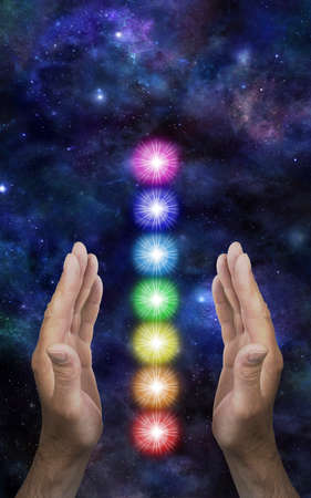 Cosmic Chakra Healing Concept - male parallel hands with a neat stack of seven rainbow coloured chakra vortexes between against a dark deep space background with copy spaceの写真素材