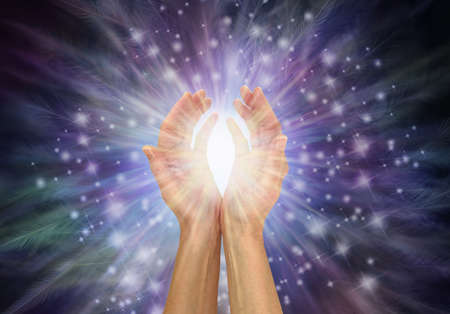 Healing Energy feels like the  beautiful tingling touch of Angel Feathers - female hands with a white healing energy burst between against radiating sparkles and feathers dark blue background with copの写真素材