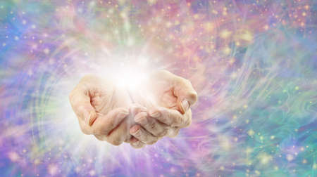Ethereal Healing Energy radiating from cupped hands - female hands cupped with white burst of light against a rotataing sparkling multicoloured energy filed, and space for text messagesの写真素材
