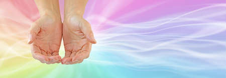 Sending out multicoloured healing energy message banner - female cupped hands against a rainbow coloured flowing background with copy space for messagesの写真素材