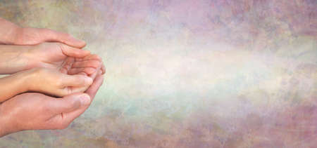 Careworker message banner background - male hands gently cupped around female cupped hands on a wide light rustic textured background with copy space for messageの写真素材