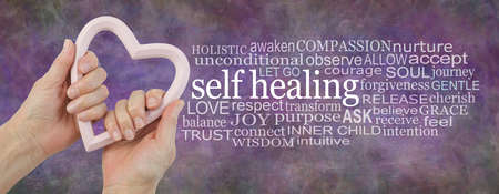 Heart-felt Self-healing word cloud background banner -  female hands holding a pink heart shaped frame beside a self healing word cloud on a rustic multicoloured backgroundの写真素材