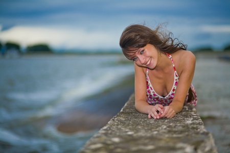 Beautiful girl in a light dress lying on a stone pierの写真素材
